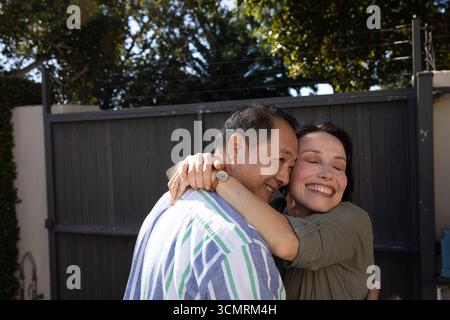 Senior couple embracing while standing at wooden gate with wristwatch and blue recycling bin Stock Photo