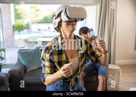 Couple playing virtual reality game in living room on sofa wearing vr headset and gesturing Stock Photo