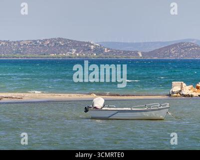 White fishing boat moored in turquoise waters with sandy beach and hills in background Stock Photo