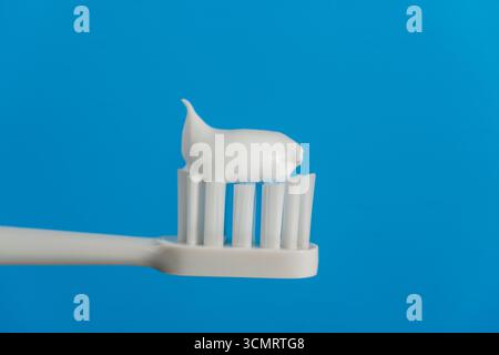 Toothpaste squeezed on the white toothbrush on blue background, close up. Dental care and hygiene tooth concept Stock Photo