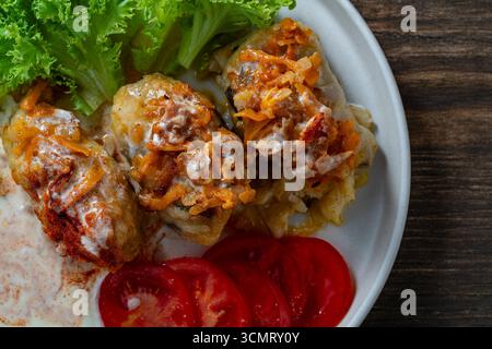 Three delicious cabbage rolls stuffed with meat and rice on a plate along with sour cream and lettuce, close up, top view Stock Photo