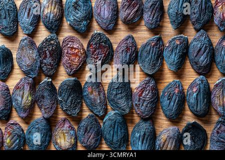Sun dried pitted plums on a wooden table, close up, top view. Background and texture of dried raw plums Stock Photo