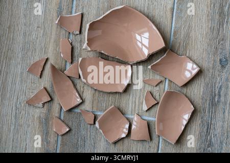 Broken ceramic beige plate on floor in kitchen, close up. Shards and pieces of a broken dish Stock Photo