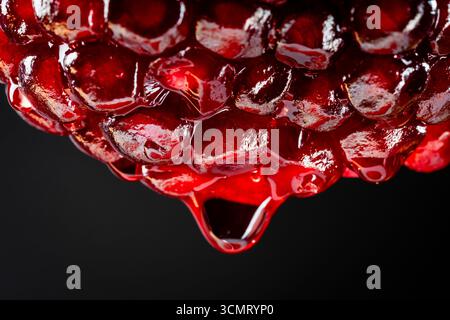 Red pomegranate juice dripping from half of fruit on black background, macro photography. Texture fresh fruit, close up Stock Photo