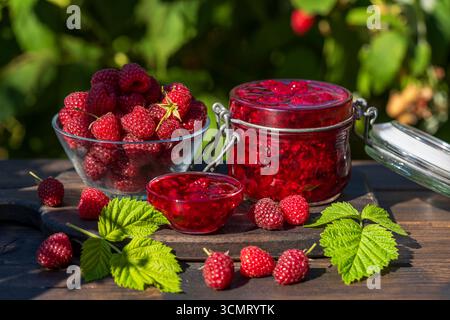 Red raspberry jam and fresh raspberry on a rustic wooden table outdoors near garden. Rustic style, close up Stock Photo