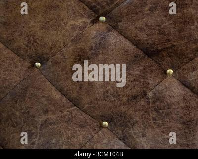 Close-up of a textured brown leather surface with diamond-tufted pattern and brass buttons. Ideal for use in interior design projects Stock Photo