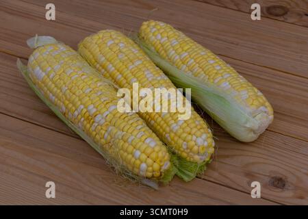 Three fresh corn cobs with husk partially removed placed on wooden table, healthy organic food and agriculture concept. Stock Photo