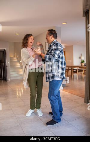 Senior couple holding hands and dancing together in living room with staircase and table Stock Photo