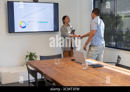 Diverse business associates shaking hands at office conference room, tablet laptop screen Stock Photo