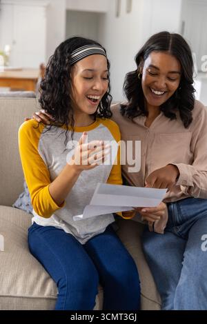 Woman explaining paperwork as teenage daughter reacting on sofa at home Stock Photo
