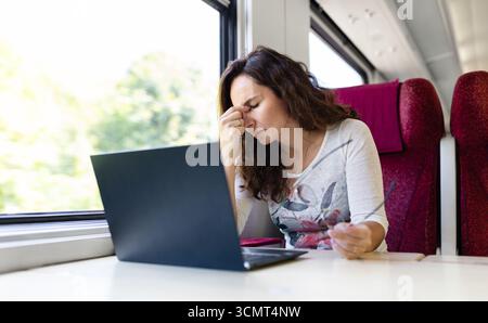 Young Caucasian woman on train feeling tired while using laptop Stock Photo