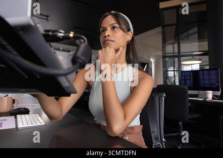 Asian woman resting chin, using stylus on pen display tablet at modern office desk Stock Photo