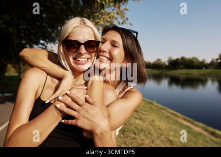 Two friends embracing and smiling outdoors by a lakeside Stock Photo