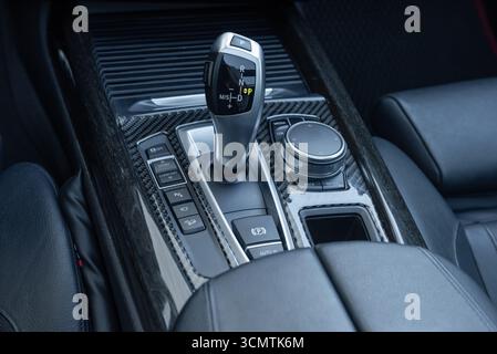 Automatic gear selector in luxury car. Automobile interior in dark tones, close-up view of bottom part of center console with lots of buttons. Stock Photo