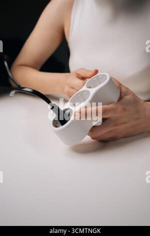 Female hands plugging black cable into white triple electrical outlet, positioned on minimalist surface with shadowy backdrop. Stock Photo