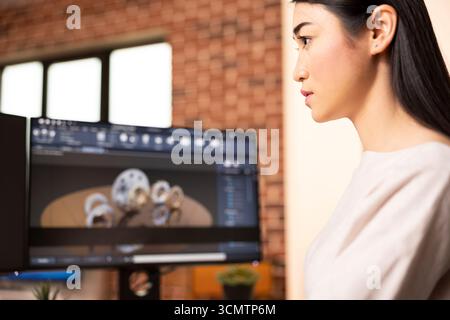 Asian woman engineer develops digital prototypes using CAD tools at home desk. Female innovator focused on construction innovation and 3D modeling workflow for precision design. Stock Photo