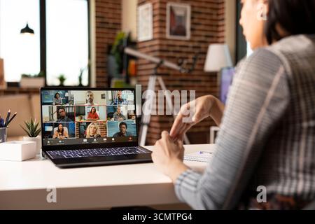 Indian female entrepreneur sits at desk with laptop, joining online workshop with multicultural team. Businesswoman works from home, presenting startup strategies to stakeholders in virtual meeting. Stock Photo
