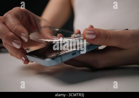 Hands of young unrecognizable woman removing broken tempered glass screen protector from mobile phone, showing importance of screen protection Stock Photo