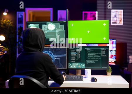 Hacker using green screen PC, coding malware designed to exploit network backdoors. Rogue engineer using mockup computer to bypass security measures such as logins and password protections Stock Photo