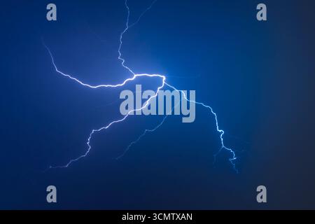 Powerful electric lightning illuminating storm clouds against deep blue night sky. Spectacular natural phenomenon captured during thunderstorm with br Stock Photo