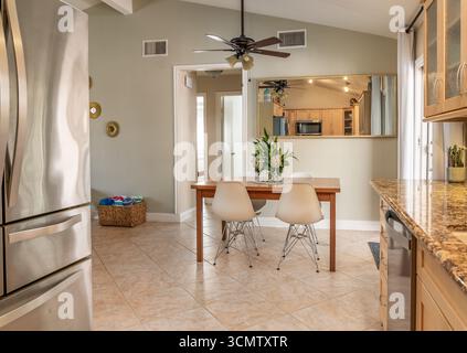 Dining table with white mid-century style chairs and bouquet of flowers next to kitchen. Stock Photo