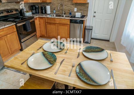 dining table set with plates silverware in modern kitchen wood cabinets top view Stock Photo
