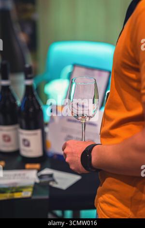 Person in an orange shirt holds an empty wine glass during a wine tasting event. Concept of wine, tasting, lifestyle centered around social gatherings Stock Photo