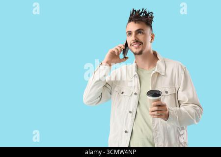 Young man with dreadlocks and coffee talking by mobile phone on blue background Stock Photo