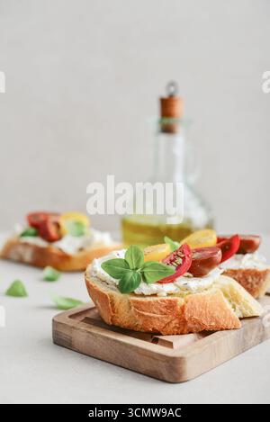 Bruschetta sandwiches with tomatoes, cream cheese, olive oil and basil on a plate on light background. Traditional italian antipasti. Stock Photo