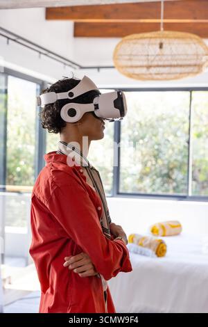Man using vr headset, standing in bedroom with beams, rattan lamp and large windows Stock Photo