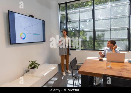 Diverse colleagues presenting data on screen in meeting room using tablet, laptop, copy space Stock Photo