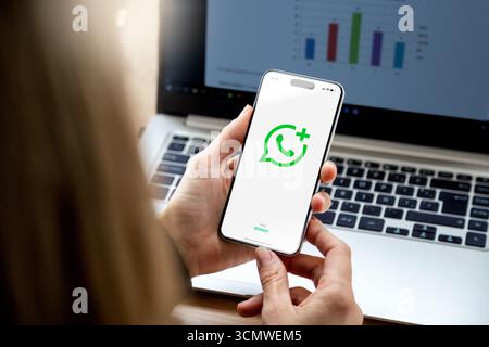 Whatsapp Business app logo on screen of mobile phone holder for a hands of young woman. Smartphone with green background display and white logotype. Stock Photo