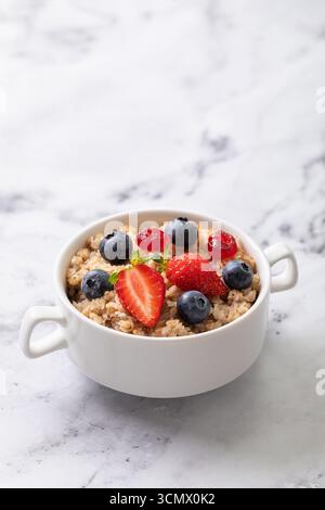 Buckwheat flakes with strawberries, blueberries and dried cherries in white ceramic plate on table with copy space Stock Photo