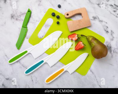 Various plastic knives and a cutting board with berries and a pear on a table, top view Stock Photo
