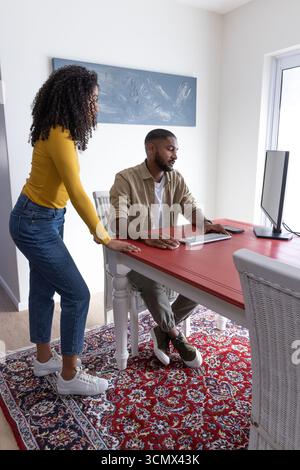 Diverse couple collaborating on desktop computer in home office corner with wooden desk Stock Photo