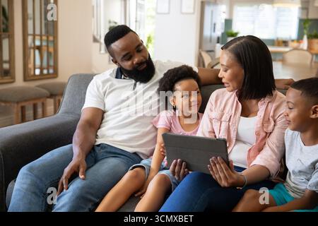 African American family sitting together and interacting with tablet on gray couch in living room Stock Photo