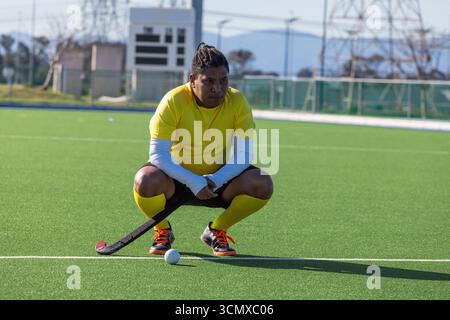 African american man crouching on turf field in yellow jersey holding hockey stick next to ball Stock Photo