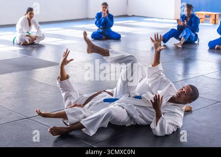 Diverse martial arts students performing ground throw on mat in training hall with white gis Stock Photo