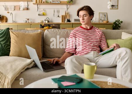 Focused student engages in e-learning while relaxing at home in the comfortable living space. Stock Photo