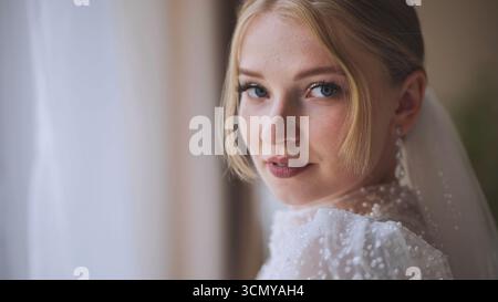 Beautiful blonde bride looking over her shoulder while wearing her white wedding dress on her wedding day Stock Photo