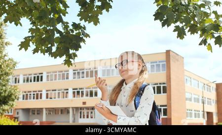 Student writing in notebook near school entrance, concentrating during academic day Stock Photo