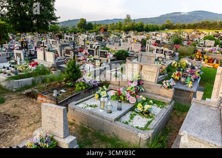 Milowka, Poland, 08.07.2021. Cemetery with traditional granite graves decorated with colorful artificial flowers and candles in Beskid Mounatins. Stock Photo