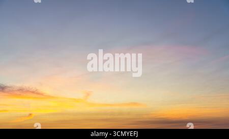 Golden and pink clouds stretch across a fading blue evening sky. Stock Photo
