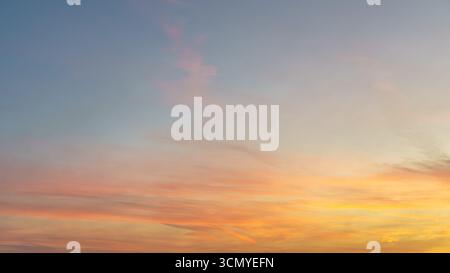 Soft orange and pink clouds drift across a pale blue evening sky. Stock Photo