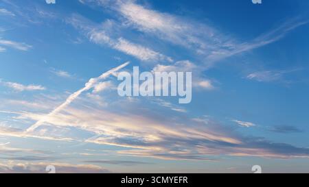 Wispy white and pink clouds streak across a bright blue sky. Stock Photo