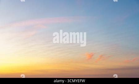 Soft pastel clouds in shades of pink and orange float under a pale blue sky. Stock Photo