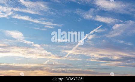 Thin white clouds and soft contrails streak across a bright blue sky. Stock Photo
