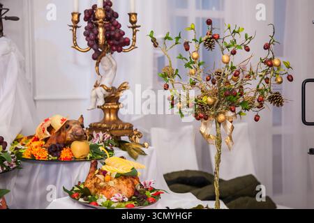 A beautifully arranged table showcases a variety of festive dishes, colorful fruits, and decorative items. The cozy indoor setting features elegant de Stock Photo