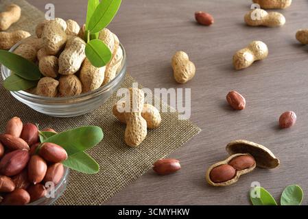 Peeled and unpeeled peanuts in glass bowls on a wooden kitchen bench. Elevated view. Stock Photo