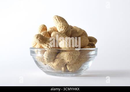 Detail of a glass bowl with a pile of peanuts in shell, isolated on white background. Front view. Stock Photo